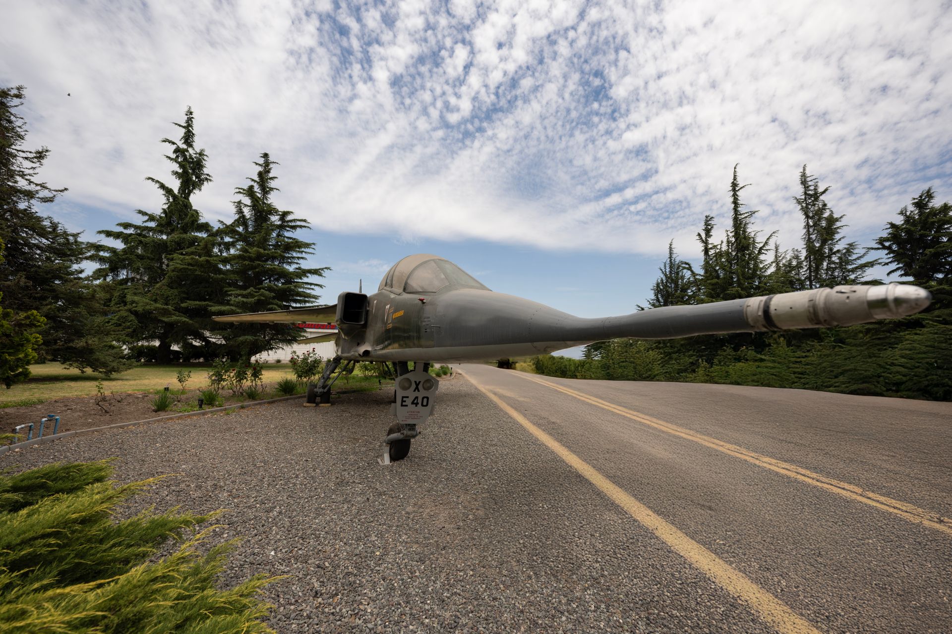 Decommissioned military jet displayed on a rural road with trees around under a cloudy sky.