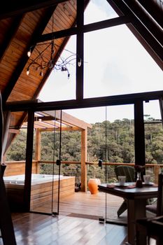 A tranquil cabin interior with large windows and hot tub overlooking a forest.