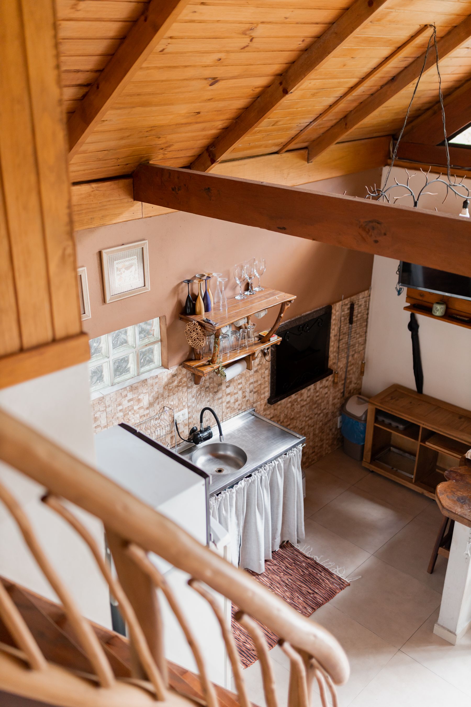 Kitchen beneath timber beams with a stainless steel sink, curtain-front storage and a small wood shelf
