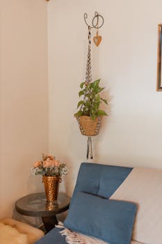 A cozy living room corner featuring a hanging plant, sofa, and side table with flowers.