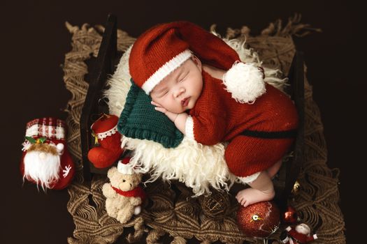 A cute newborn baby dressed as Santa Claus sleeps on a cozy setup with festive Christmas decor.