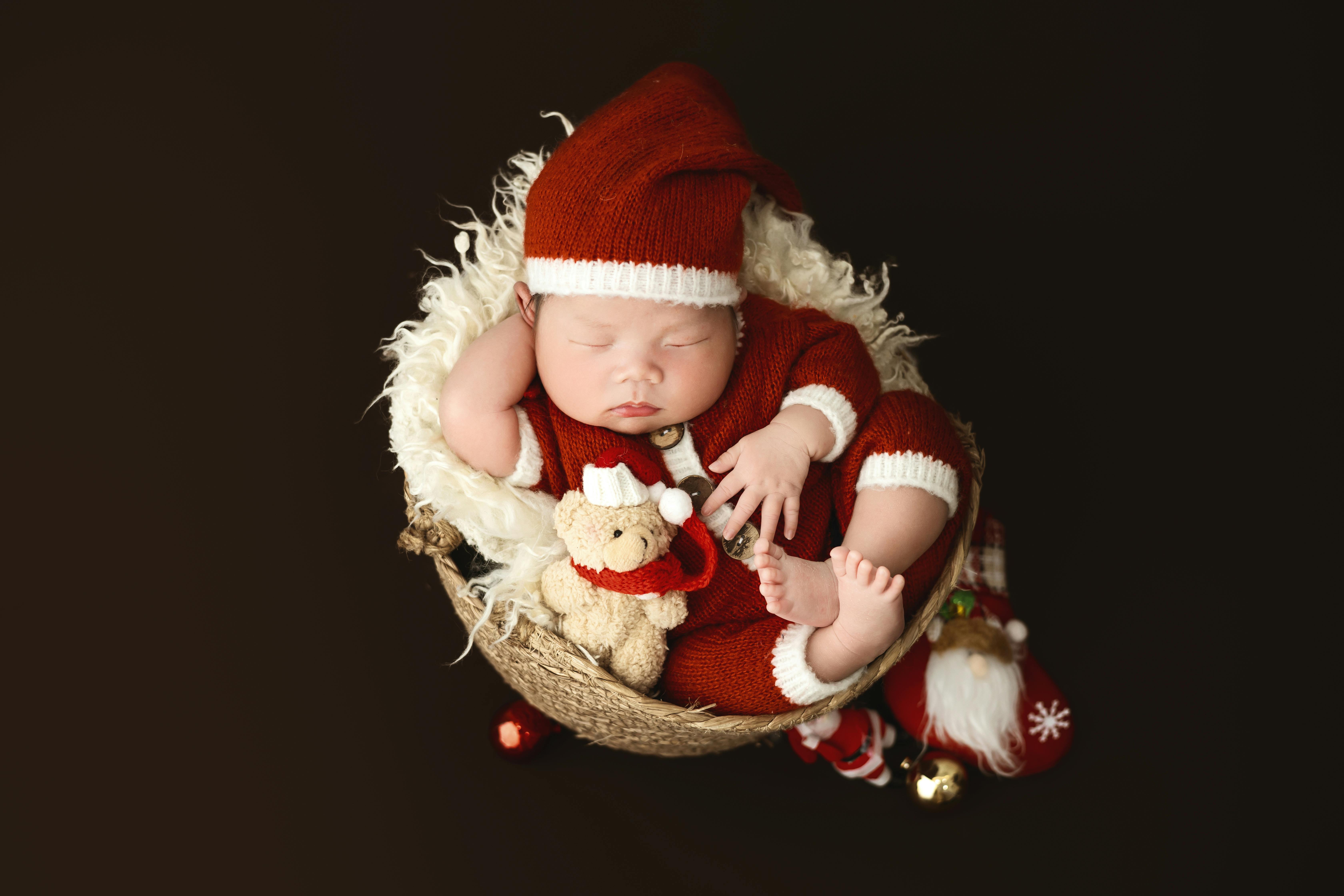 Adorable sleeping newborn in Santa outfit with Christmas toys, perfect for festive themes.
