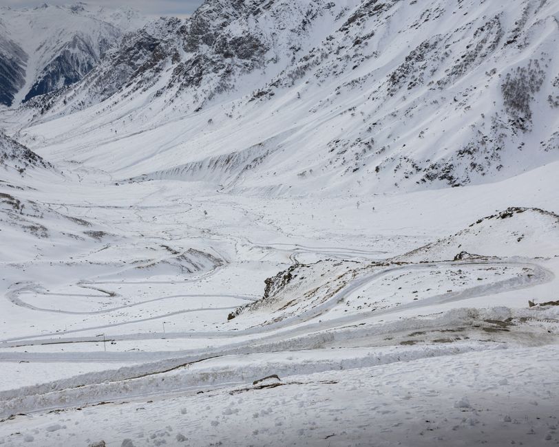 A breathtaking landscape of snow-covered mountains with winding roads under a winter sky.