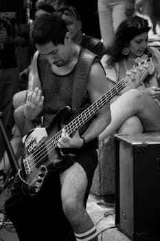 Black and white photo of a bass guitarist in a street performance, emphasizing urban music culture.