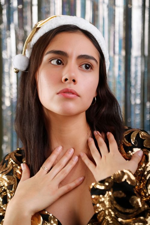 Free Charming woman in Santa hat and gold dress looking thoughtful indoors. Stock Photo