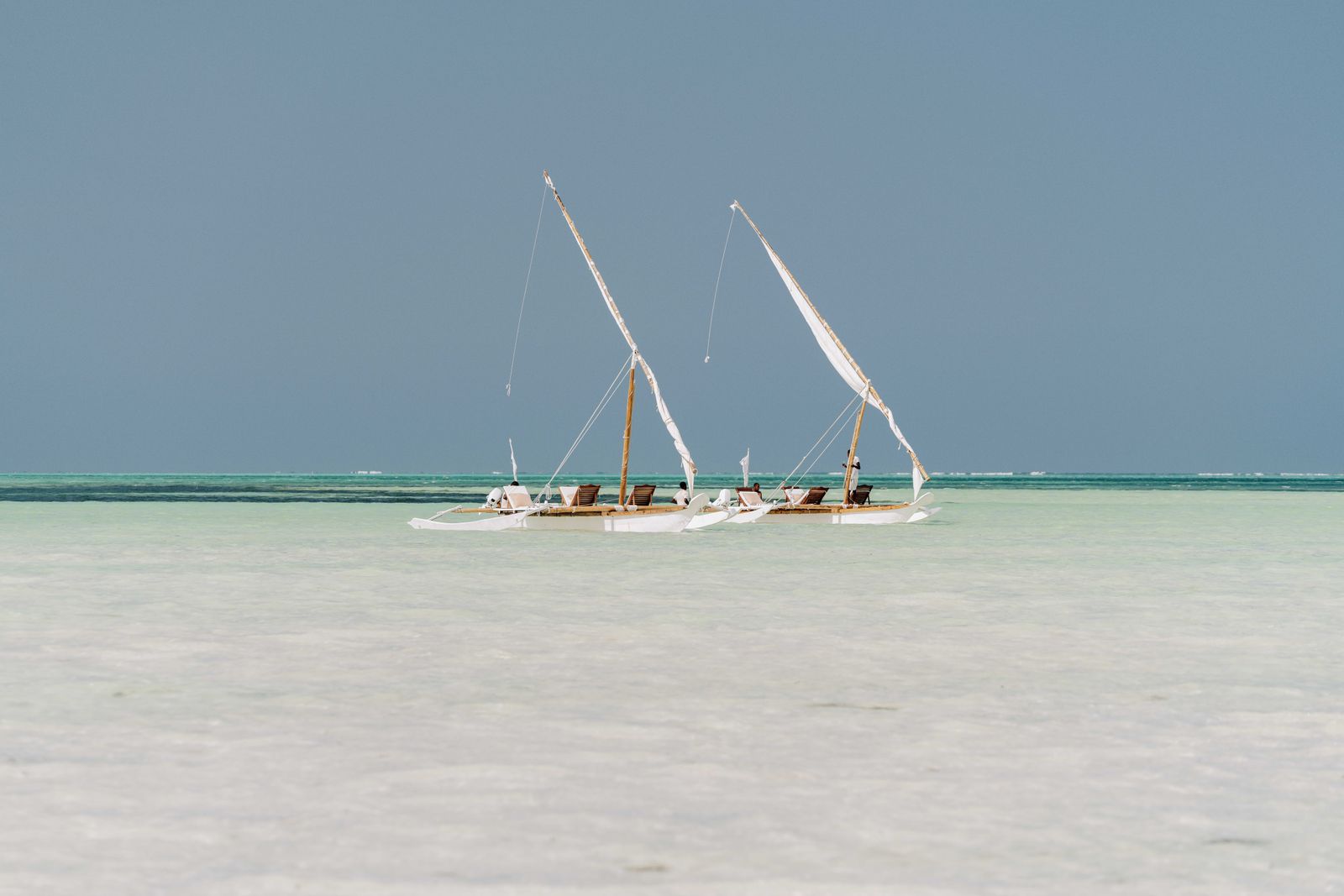 Plage de sable blanc à Zanzibar avec eau turquoise et bateau traditionnel dhow à l'horizon