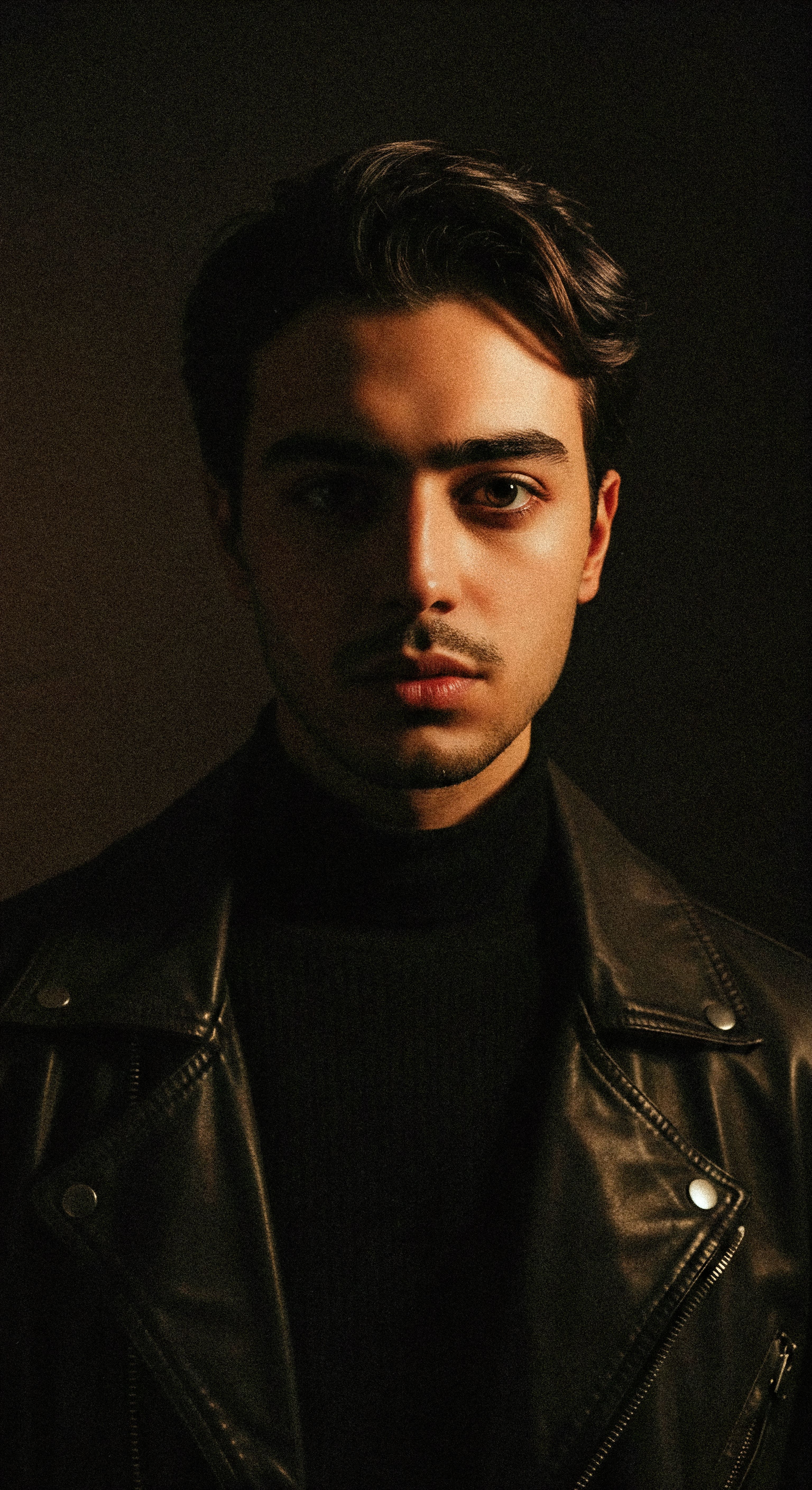 Dramatic portrait of a man in a leather jacket under warm lighting.