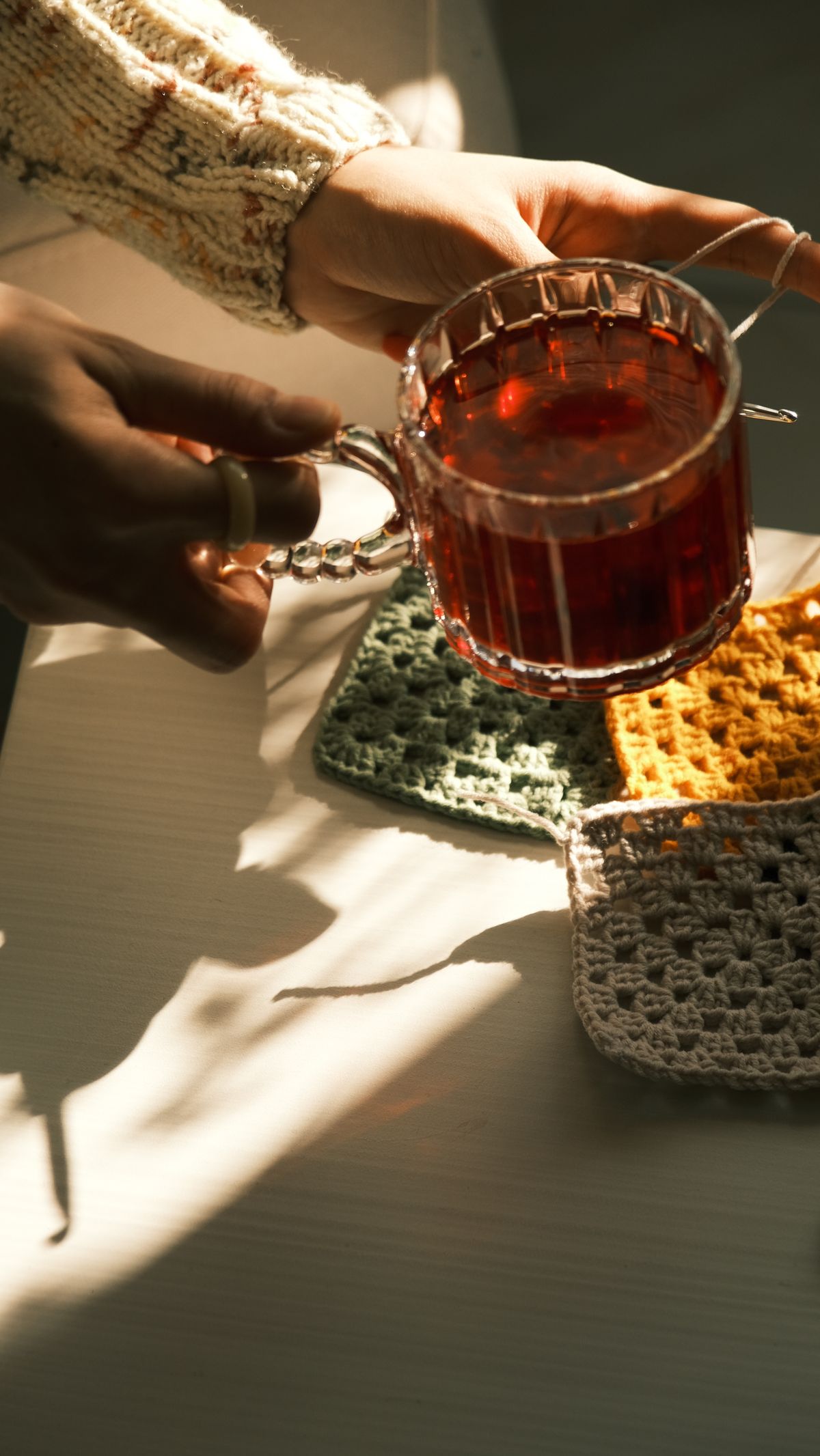 Warm sunlight on hands holding tea with crochet coasters. Perfect for cozy moments.