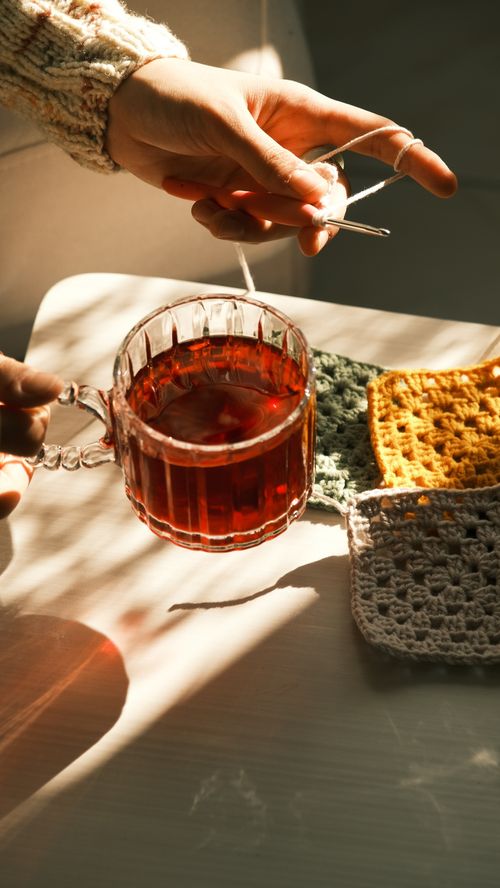 Free Warm sunlight on handmade crochet pieces and a cup of herbal tea, evoking cozy vibes. Stock Photo