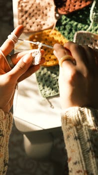 Detailed view of hands crocheting colorful squares by sunlight.