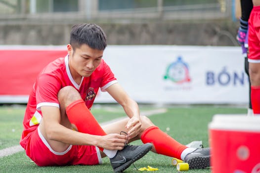 Soccer player tying shoelaces on the field pre-match in Hanoi, Vietnam.