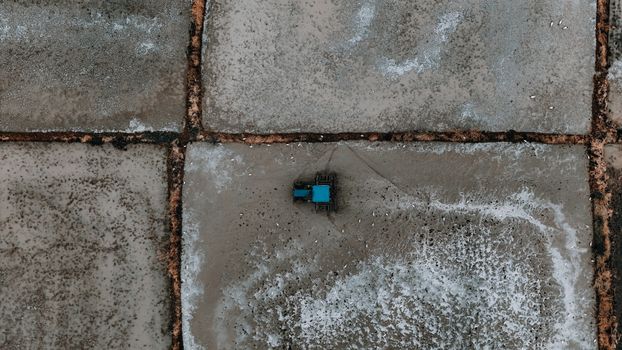 Drone shot of a blue tractor on geometric salt flats, showcasing farming in a unique landscape.