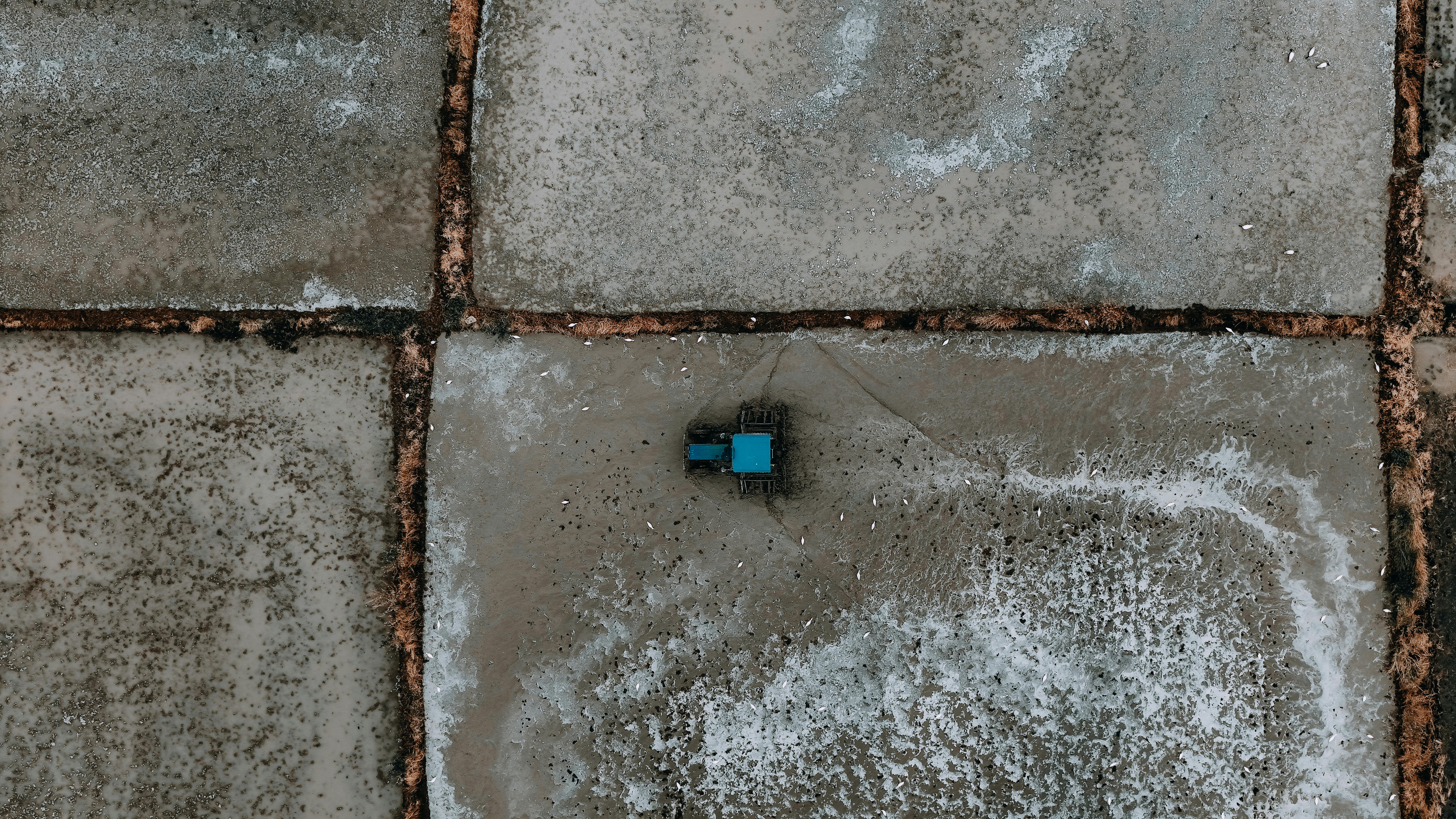 Free Drone shot of a blue tractor on geometric salt flats, showcasing farming in a unique landscape. Stock Photo