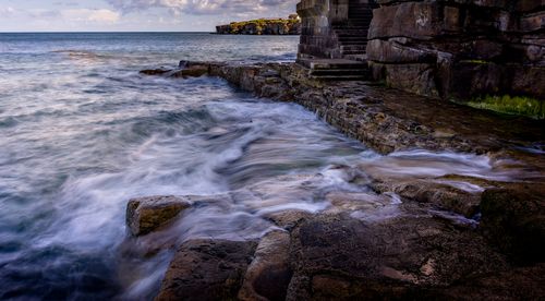 Free Waves crash against a rugged rocky shoreline with overcast skies, showcasing nature's raw beauty. Stock Photo