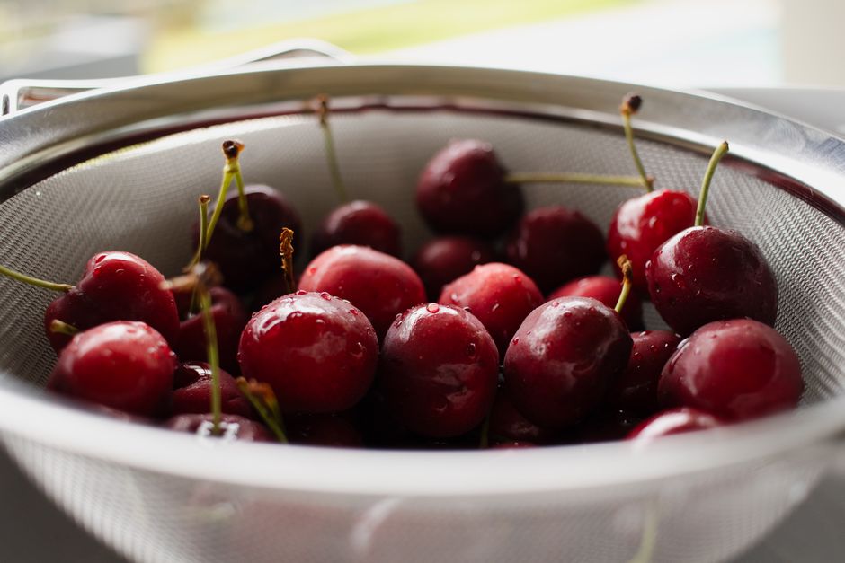 Close-up of fresh wet cherries resting in a metal colander, indoors.