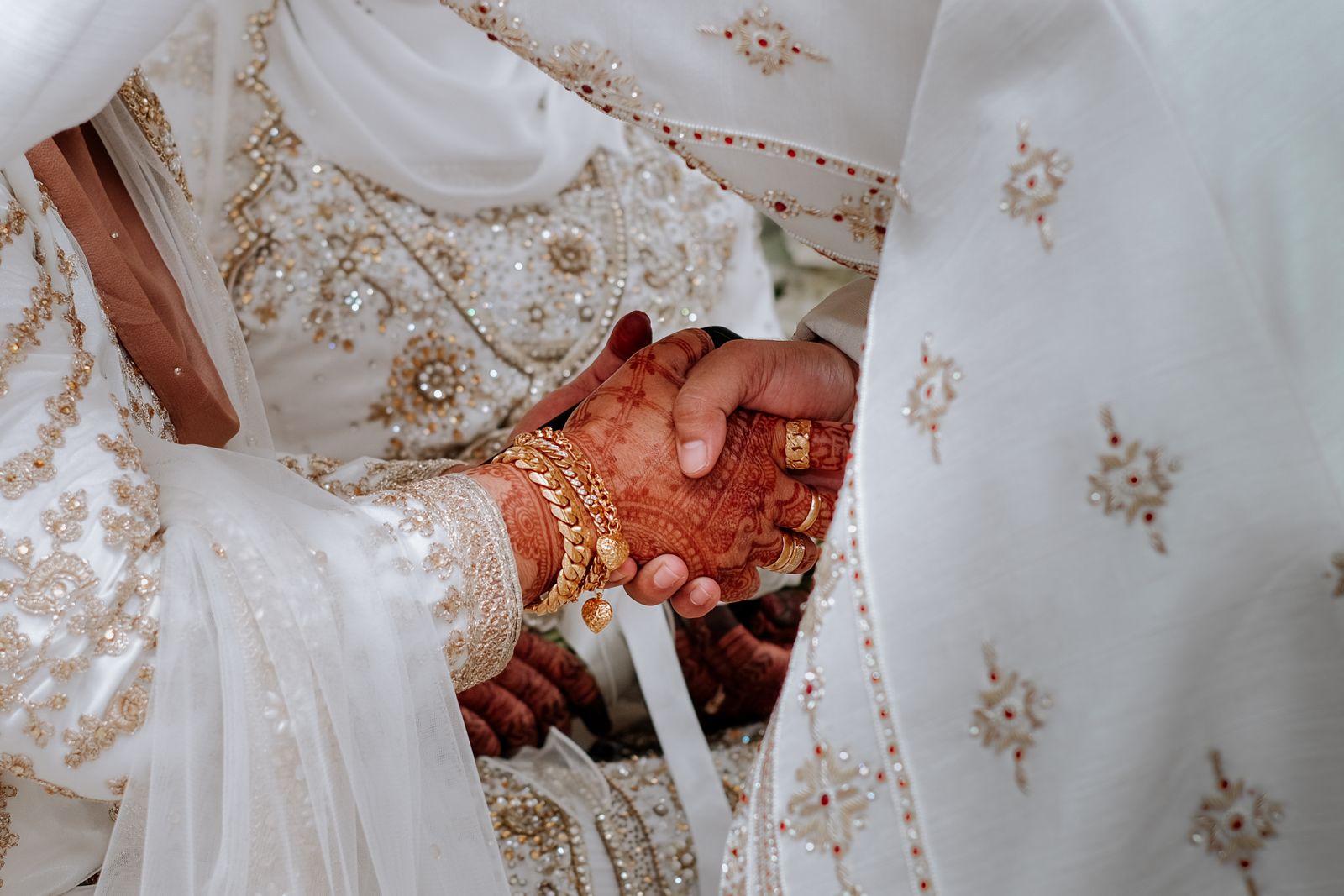 Two mehndi covered hands clasped over ivory and gold bridal fabric.