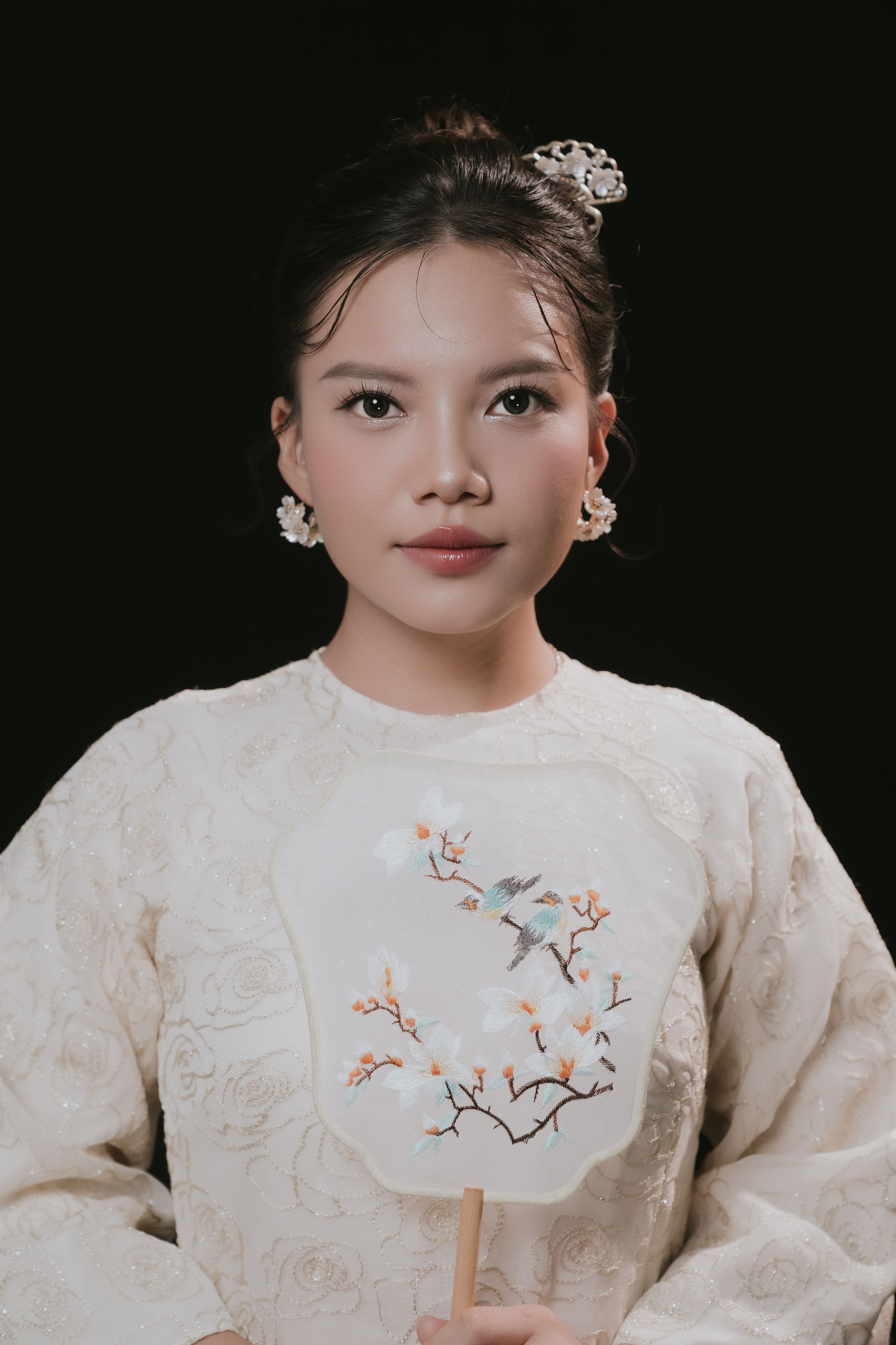 Portrait of a woman in traditional clothing holding an intricately embroidered fan against a dark background.