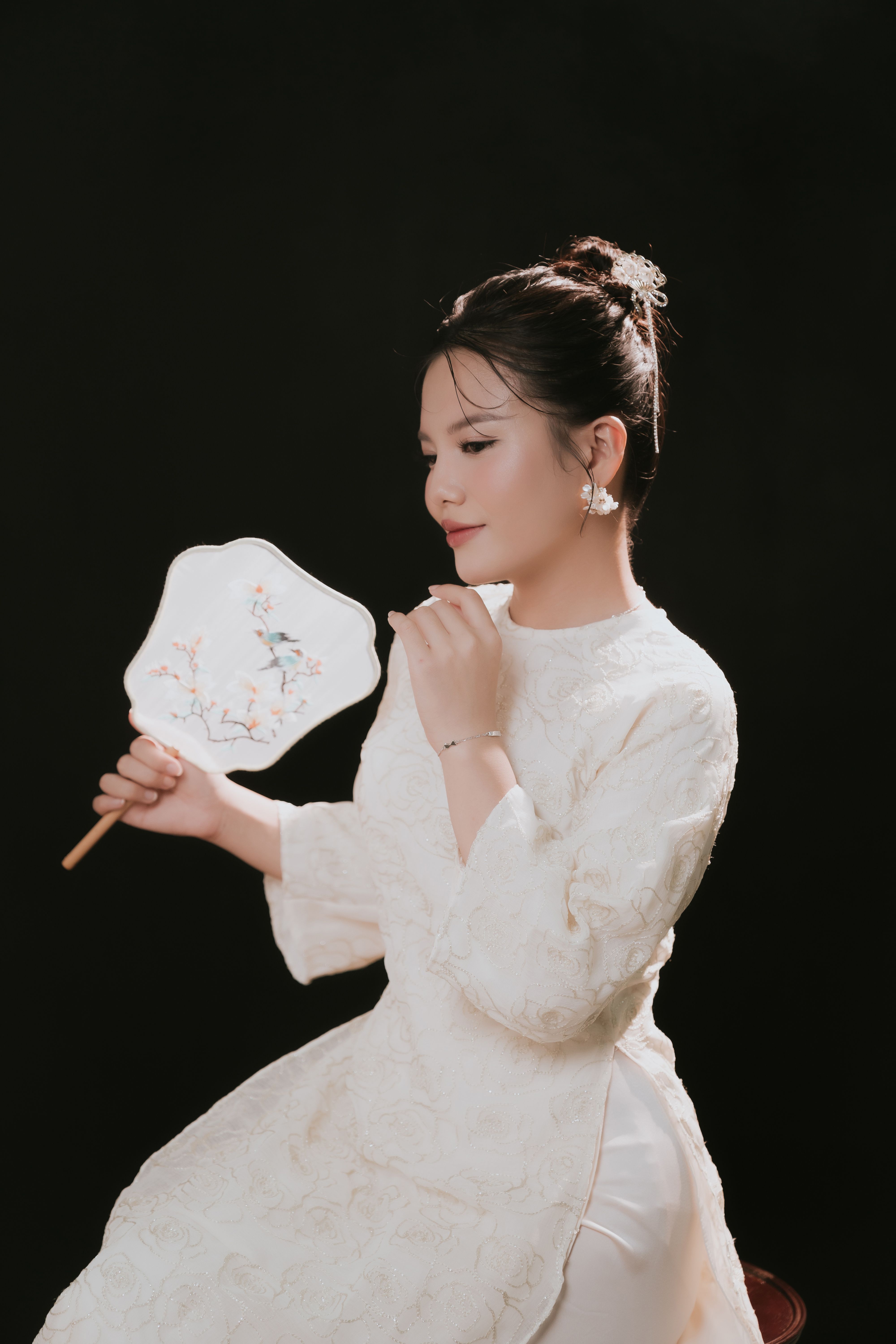 Portrait of an elegant woman in a long traditional dress holding a decorative fan.