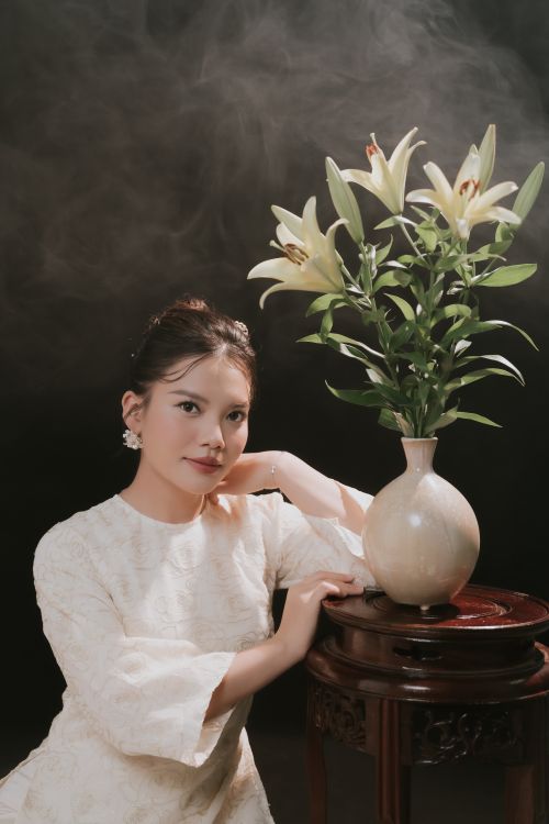 Free Woman in elegant dress posing beside a vase of white lilies indoors. Stock Photo