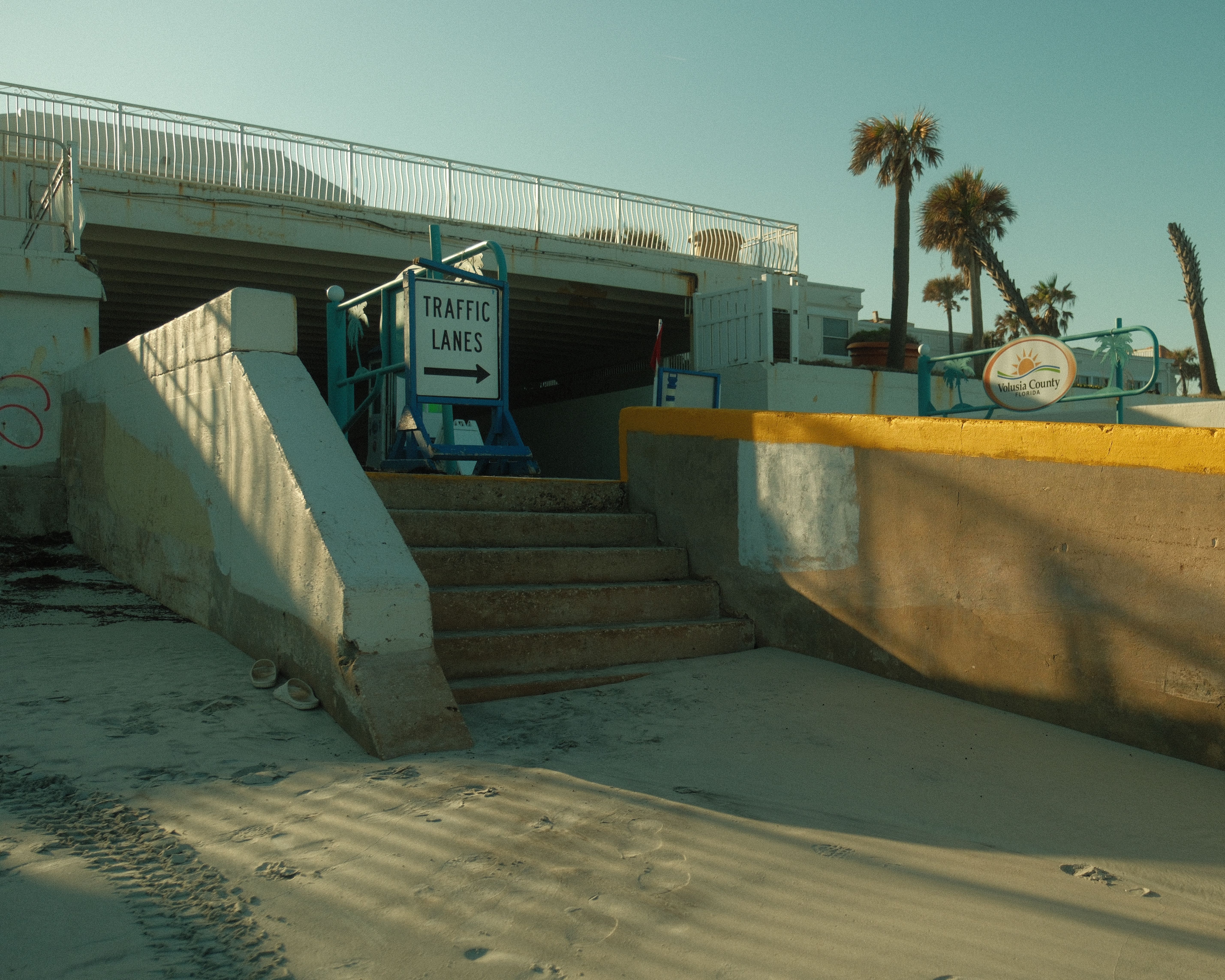 Traffic lanes sign near beach stairs and palm trees in afternoon light.