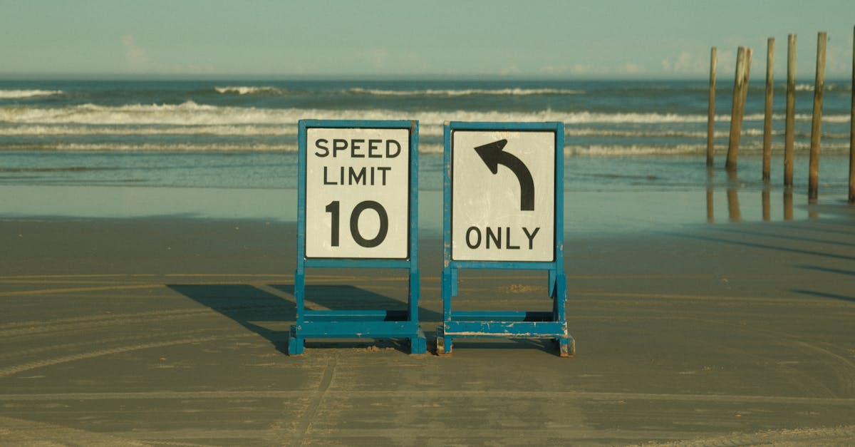 Beach scene with speed limit and left turn signs on the sand, ocean backdrop.