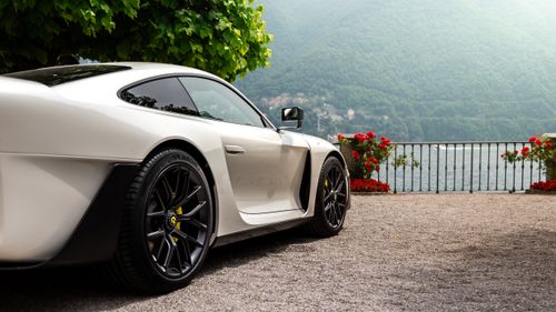 Free A sleek luxury sports car parked by a picturesque lake surrounded by lush greenery. Stock Photo
