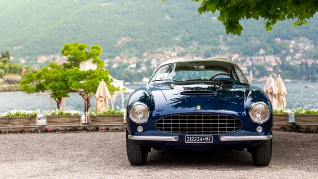 Elegant vintage blue car parked by a picturesque lake, showcasing luxury and classic design.