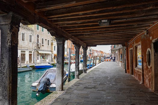 Picturesque view of a canal in Murano, Italy, with rustic buildings and boats lining the waterway.