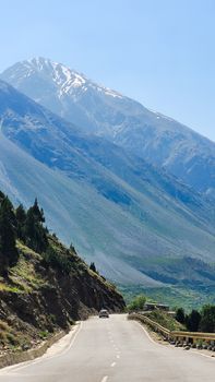 A breathtaking view of a mountain road leading towards a snow-capped peak under a bright blue sky.