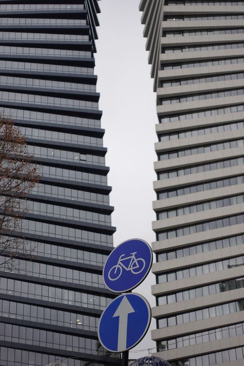 Free View of two modern skyscrapers with a blue bicycle path sign in the foreground. Stock Photo