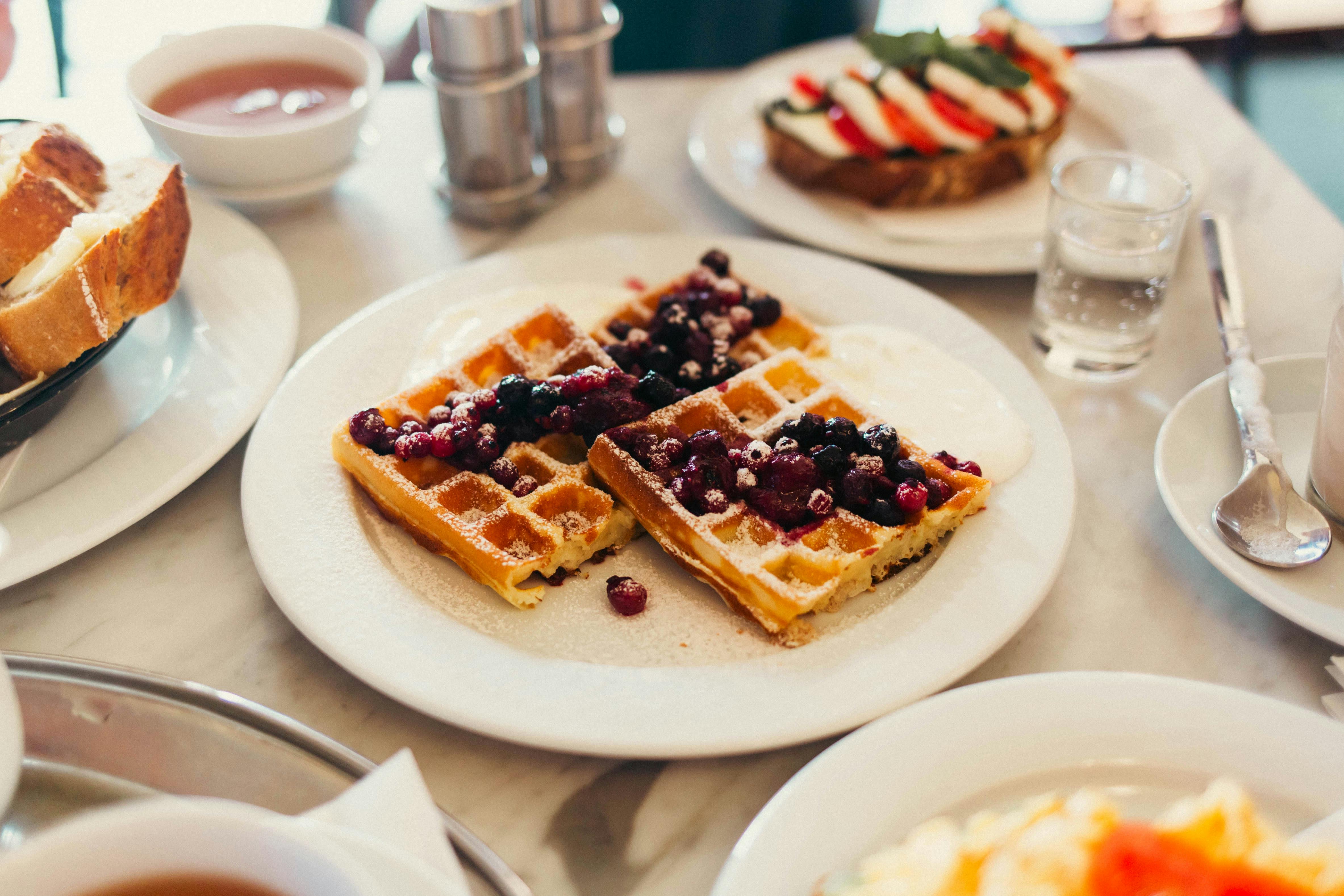 Plate of waffles with berries and cream at a cozy breakfast setup.