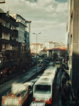 Bustling city street view with blurred traffic and tall buildings under a cloudy sky.