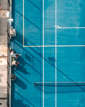 Top-down view of a blue tennis court in Miami, showcasing players and shadow play under bright sunlight.