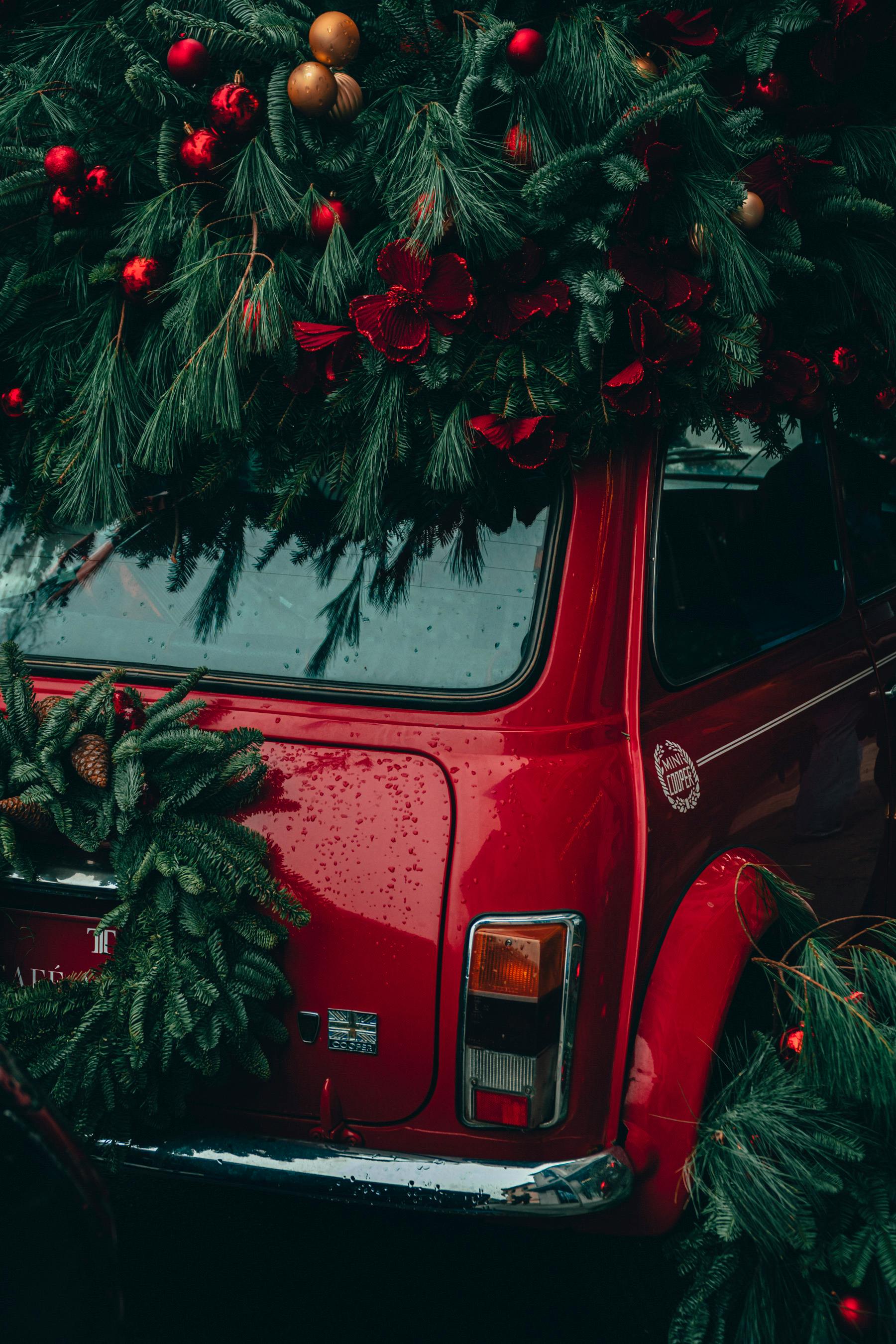 Classic red car adorned with evergreen and festive ornaments, embodying holiday spirit.