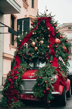 Old car adorned with a Christmas tree, red ribbons, and ornaments in a charming street.