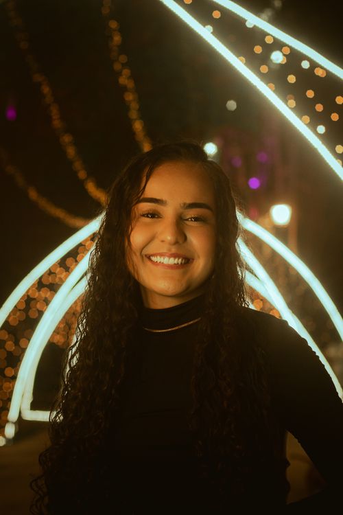 Free Portrait of a woman smiling under decorative festoon lights at night. Stock Photo