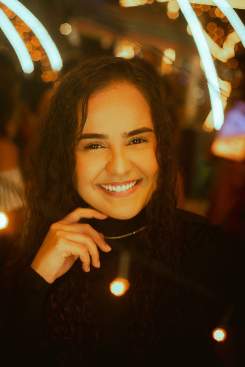 Free A cheerful woman smiling surrounded by warm, festive lights at night. Stock Photo