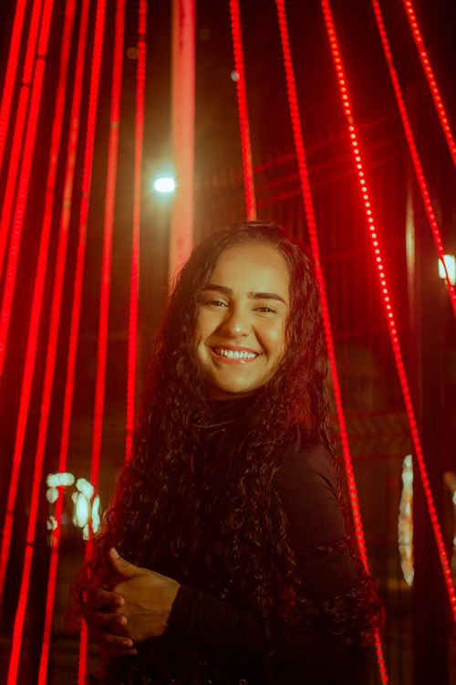 Free A joyful woman with curly hair smiles brightly under dramatic red lights at night. Stock Photo