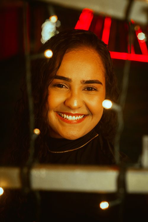 Free A joyful woman smiling surrounded by warm string lights, creating a festive atmosphere. Stock Photo
