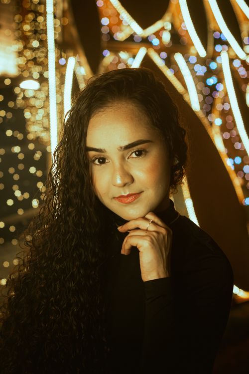 Free Captivating portrait of a woman with long curly hair against a backdrop of bokeh festive lights. Stock Photo
