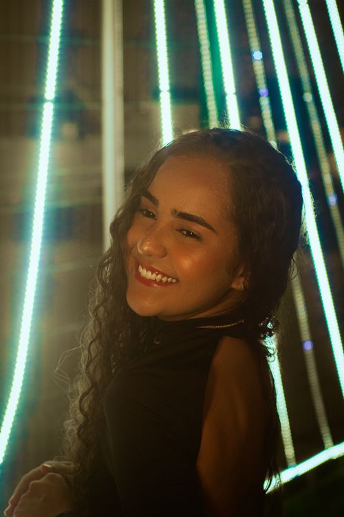 Free A woman with curly hair smiling warmly in front of neon lights, exuding joy and warmth. Stock Photo