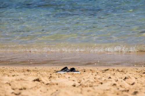 Free A peaceful beach scene with flip flops resting on the sandy shore near gentle waves. Stock Photo