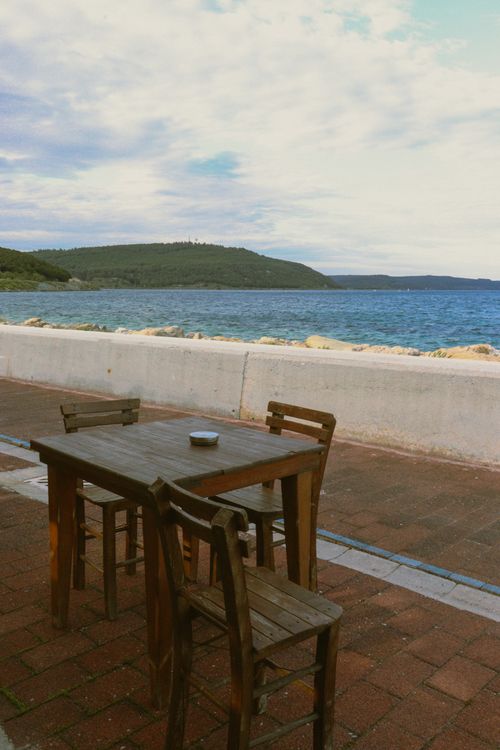 Free Wooden chairs and table set against a beautiful seaside backdrop, perfect for relaxation. Stock Photo