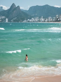Woman enjoying the vibrant waves at Ipanema Beach, overlooking the stunning Rio skyline and mountains.