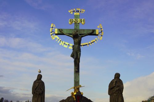 Free Crucifixion statue with Hebrew inscription and two figures under a vivid sky, located outdoors. Stock Photo
