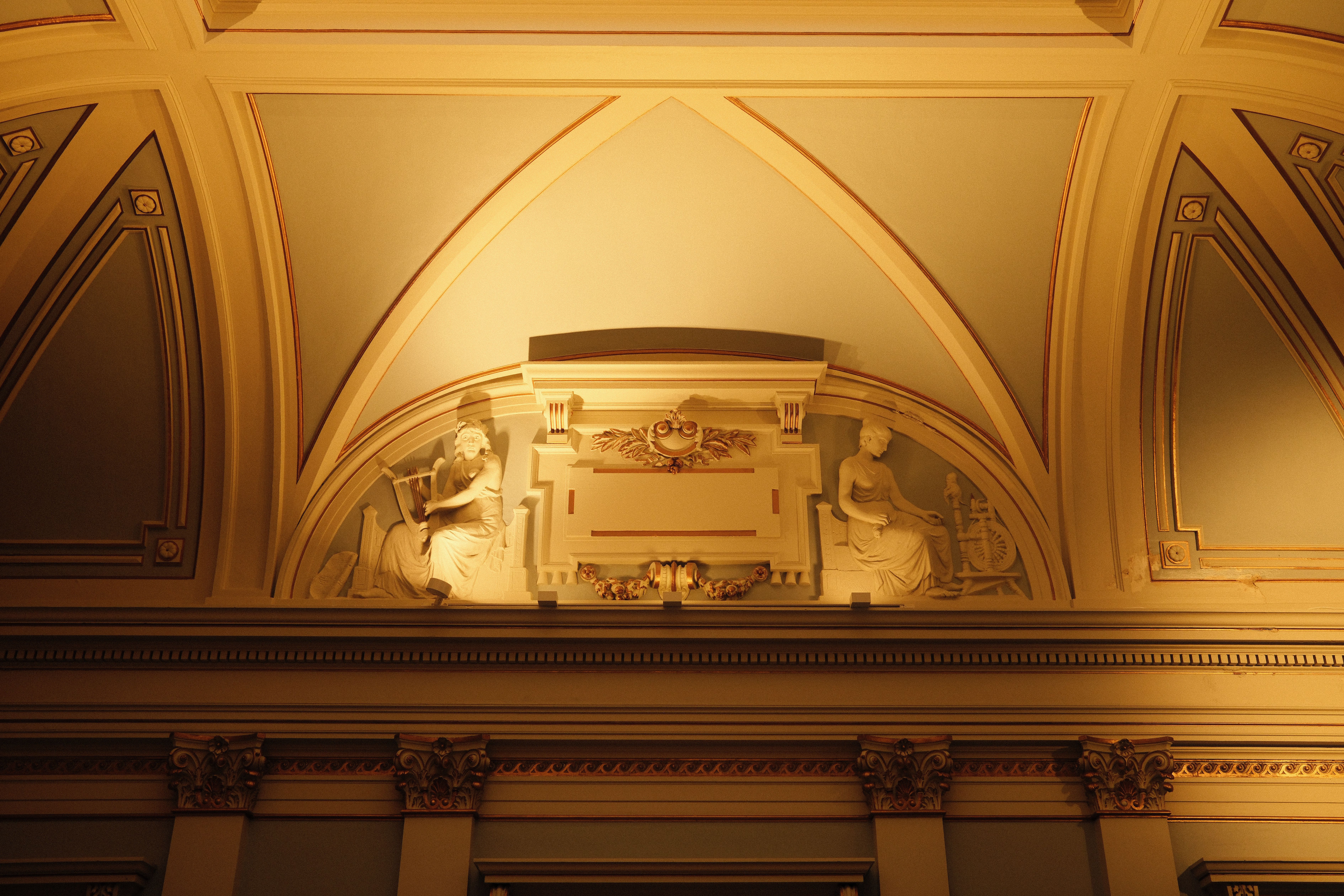 An ornate ceiling with classical sculptures in soft, warm lighting.