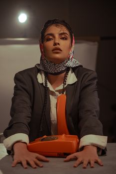 Retro-styled woman in a scarf and suit with a vintage orange phone.