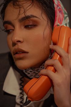 Close-up of a woman in a headscarf holding a vintage orange phone.