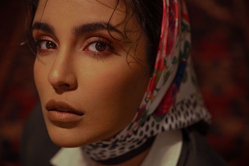 Free Close-up portrait of a woman wearing a colorful floral headscarf, capturing a warm and mysterious expression. Stock Photo