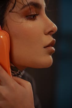 Close-up of stylish woman talking on an orange rotary phone with vintage vibe.